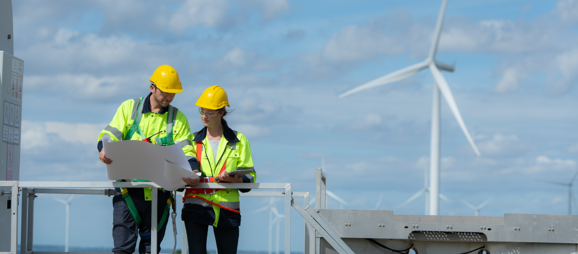 Two engineers checking schematics in front of a wind farm